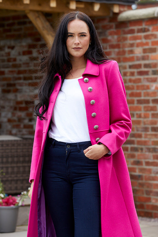 Model wearing a pure wool bright pink , single breasted coat with silver buttons