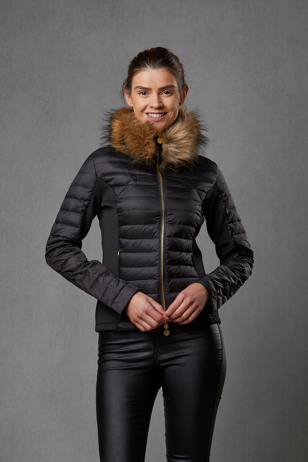 Model wearing a women's down padded jacket in black with stretch sides. The jacket has a detachable faux fur collar and branded gold zip.