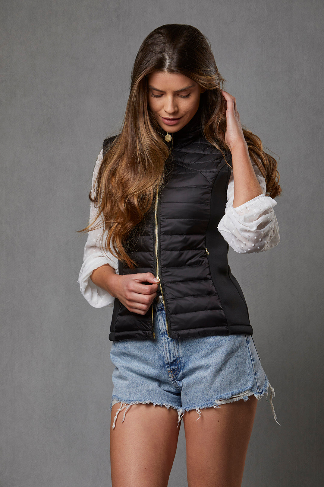Model wearing a women's puffer gilet with shorts. The detachable faux collar has been removed to show the garment for a more summery look