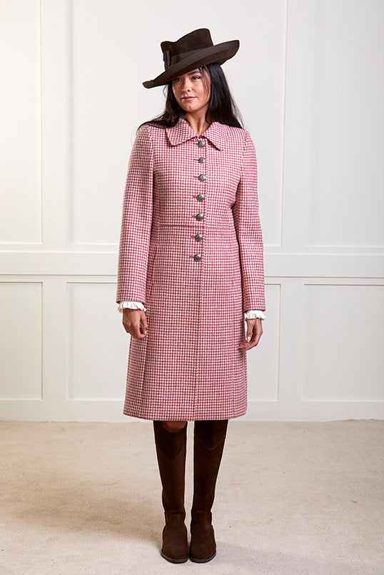 Model wearing a pure wool, single breasted coat in small pinky, red and cream check. The coat has 7 silver buttons.