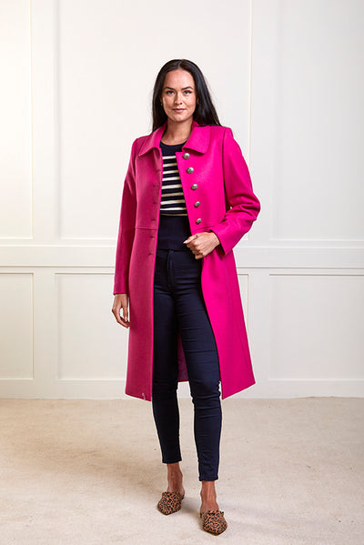 Model wearing a pure wool bright pink , single breasted coat with silver buttons