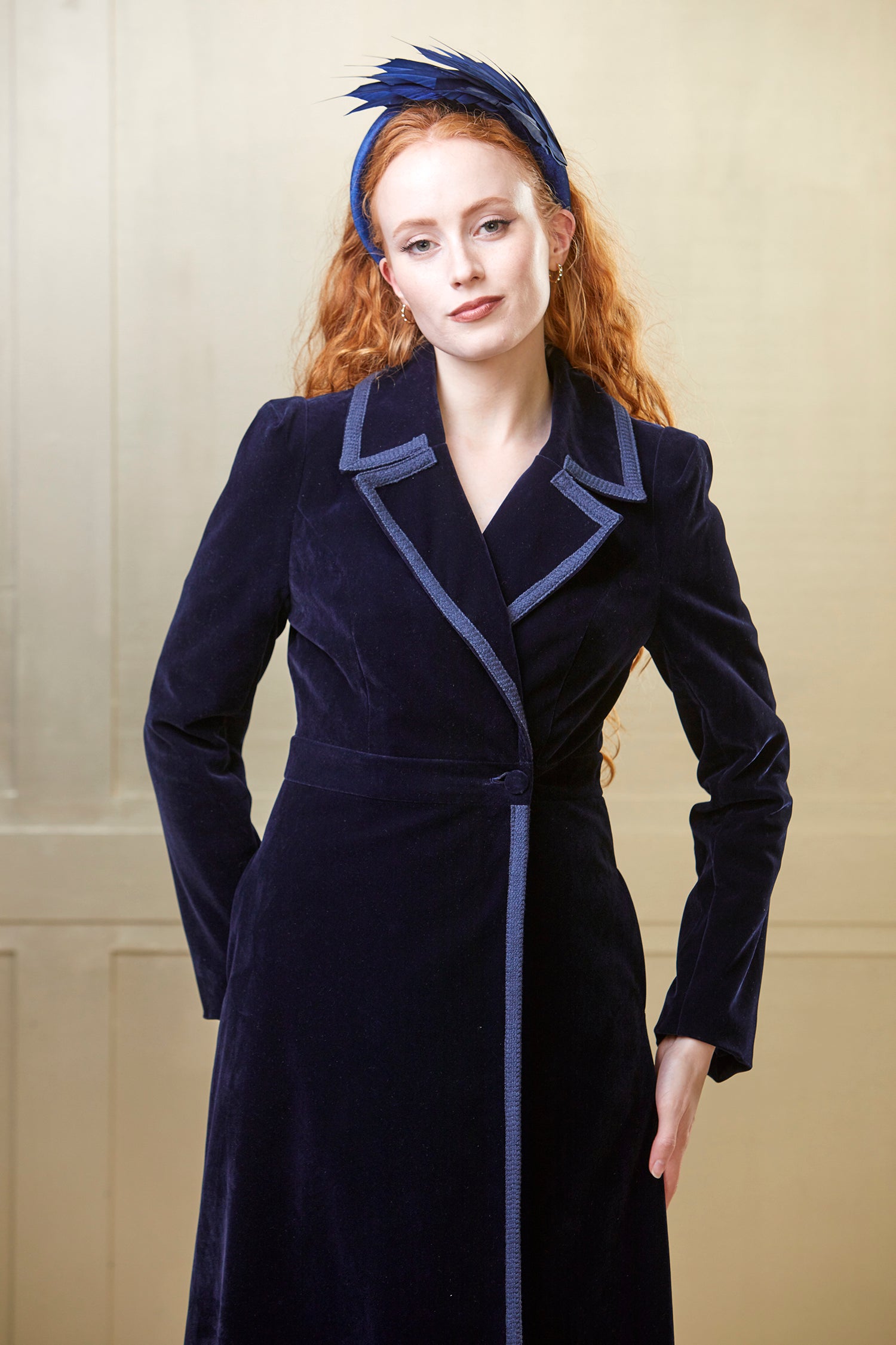 A navy blue velvet coat dress with braid trims. The coat dress is accessorised for a wedding look with a matching headband.