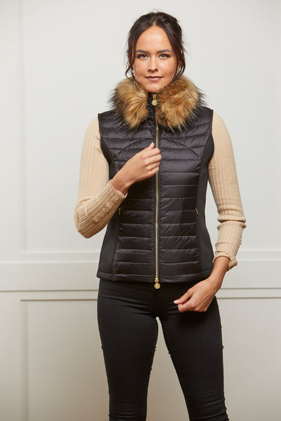 Model wearing a women's padded gilet in black with stretch sides and a detachable faux fur collar and zip front.