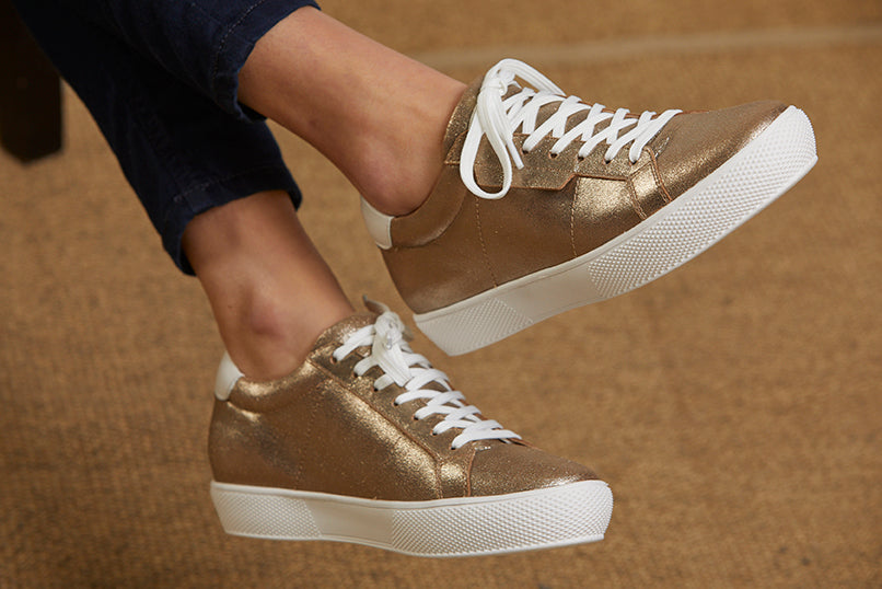 Model wearing a women's low top leather trainer in bronze gold with white laces and trims